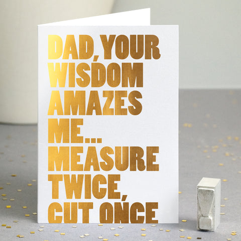 A funny gold foiled greetings card with the quote 'dad, your wisdom amazes me... measure twice, cut once. Part of the text is cut off at the bottom of the card.