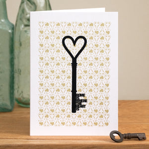 A housewarming card with a key silhouette and the words 'home is where the heart is' forming the key blade.